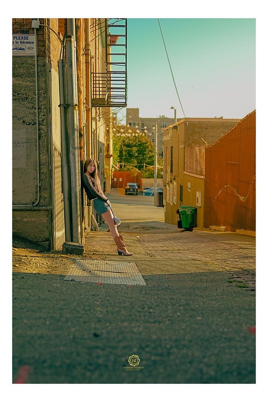 Model leaning against a wall in a sunlit alley