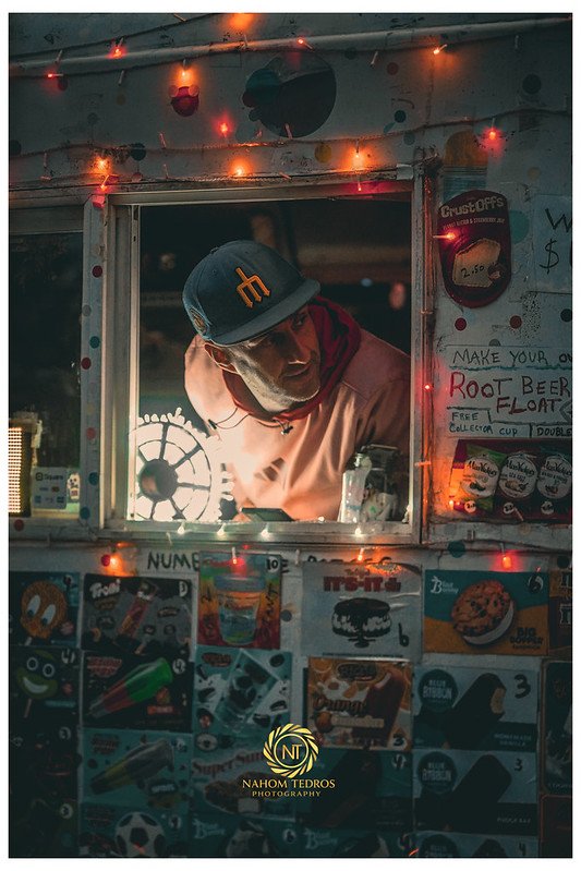 Man in a cap at a string-light food truck window
